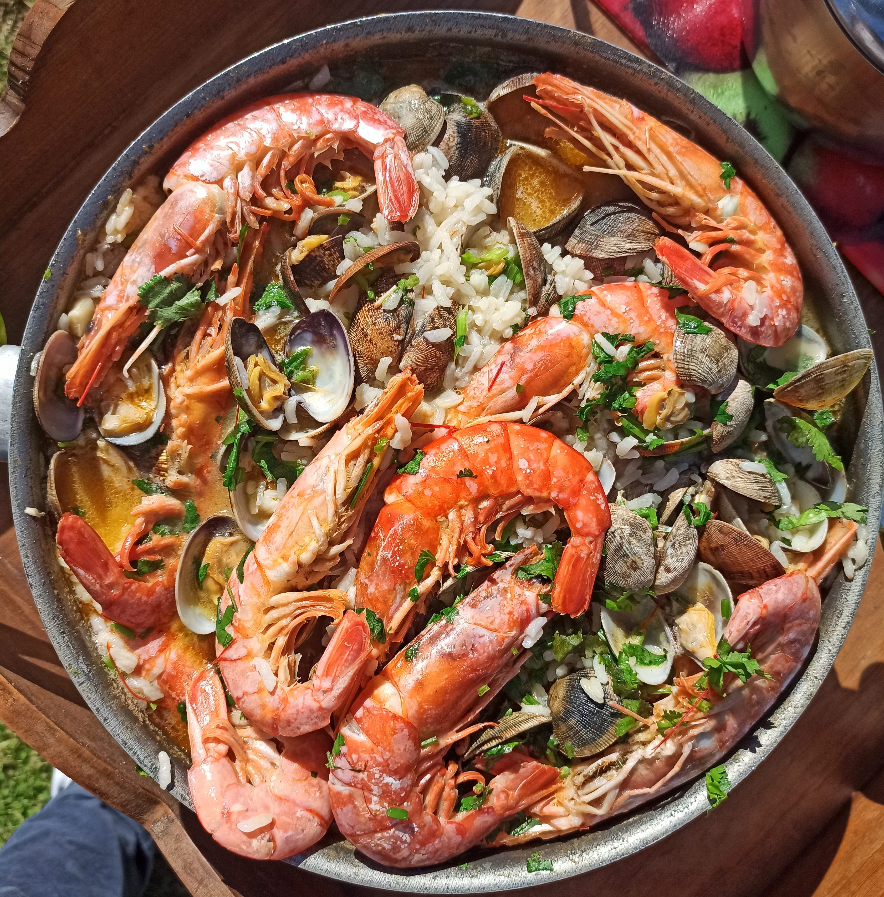 A close-up shot of a seafood dish featuring large shrimp and clams served over rice, garnished with fresh parsley.
